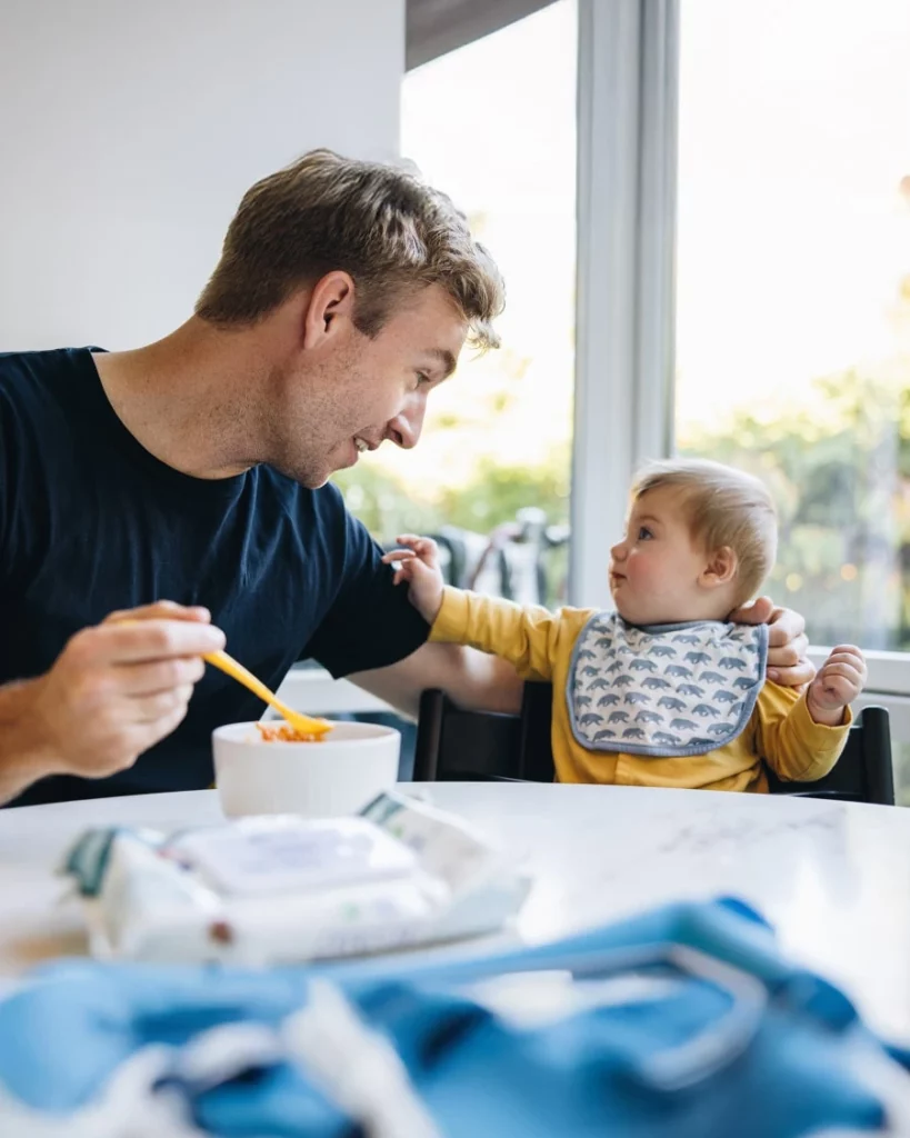 Zavádíme příkrmy: táta nabízí miminku jídlo u společného stolu.